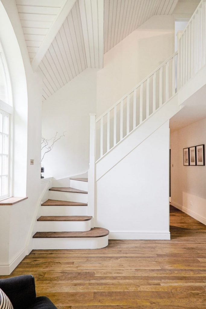 Light-filled entrance hall with white staircase, timber treads and vaulted ceiling in a contemporary Buckinghamshire family home.