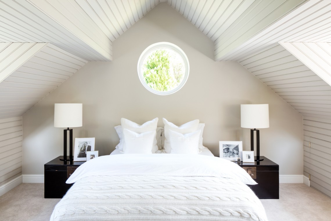 Serene loft bedroom with vaulted white panelled ceiling, circular window and symmetrical bedside styling.
