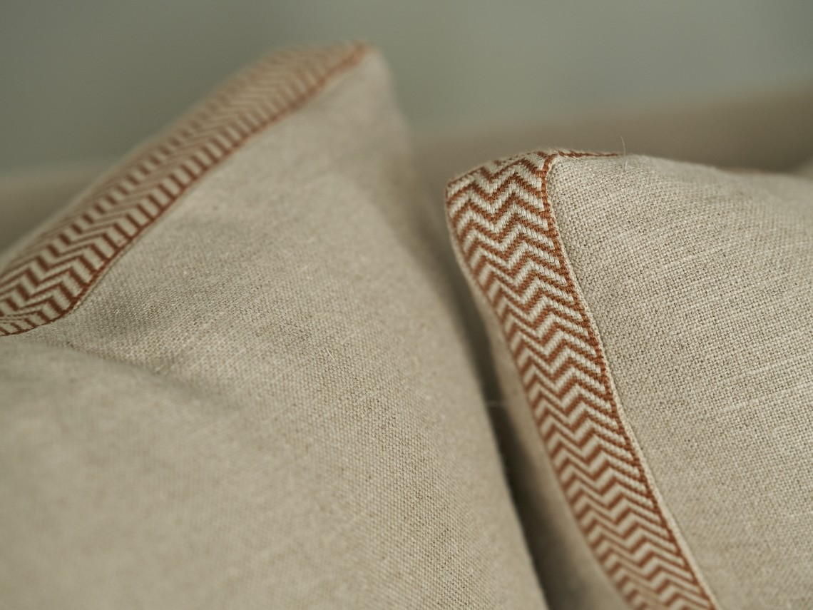 Close-up detail of neutral linen cushions finished with terracotta herringbone trim, highlighting tailored upholstery and refined textural contrast.