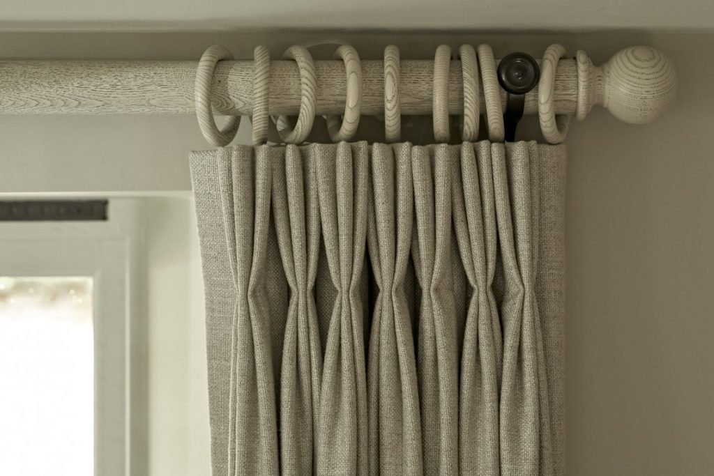 Close-up of bespoke curtain detailing in a Cotswold country retreat, featuring soft neutral linen curtains hung from a handcrafted wooden pole with oversized hand-turned rings.