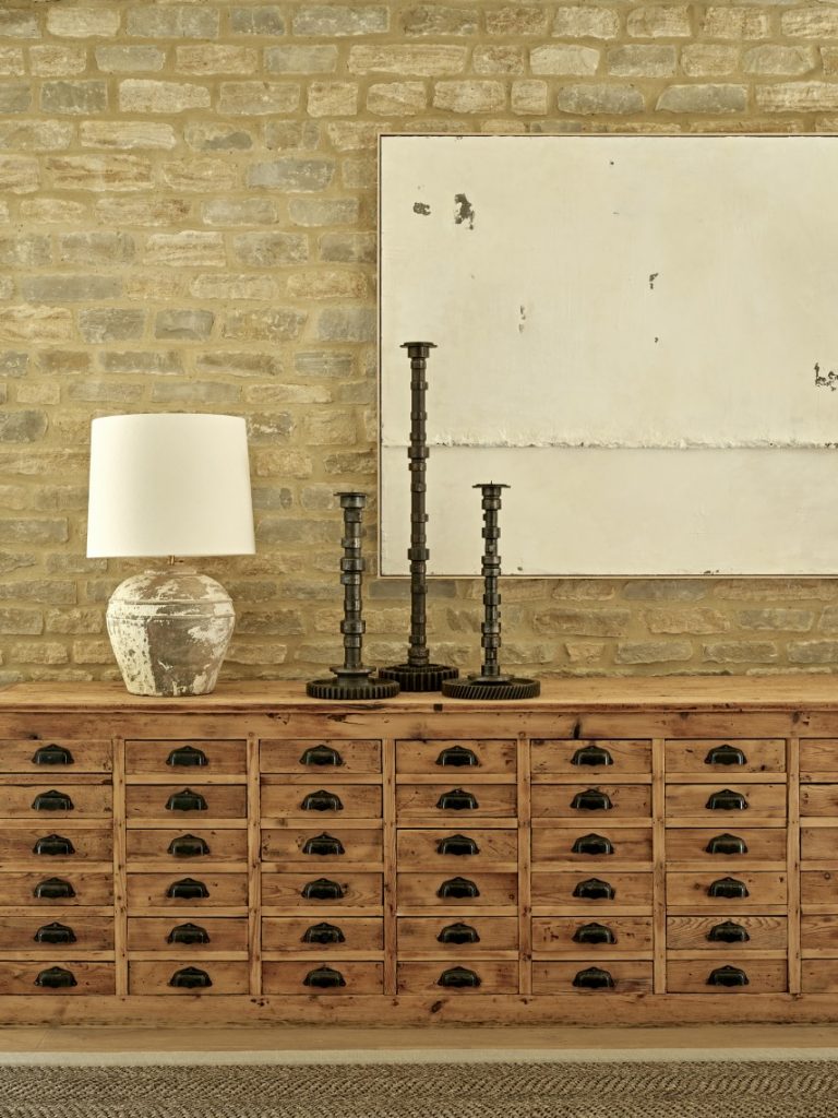 Antique apothecary cabinet styled against exposed Cotswold stone in a converted barn interior.