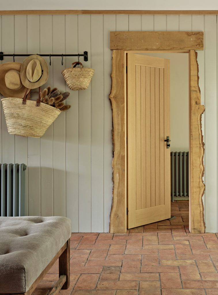 Entrance hall in a Cotswold barn conversion with an oak door, terracotta floor tiles and painted panelling.