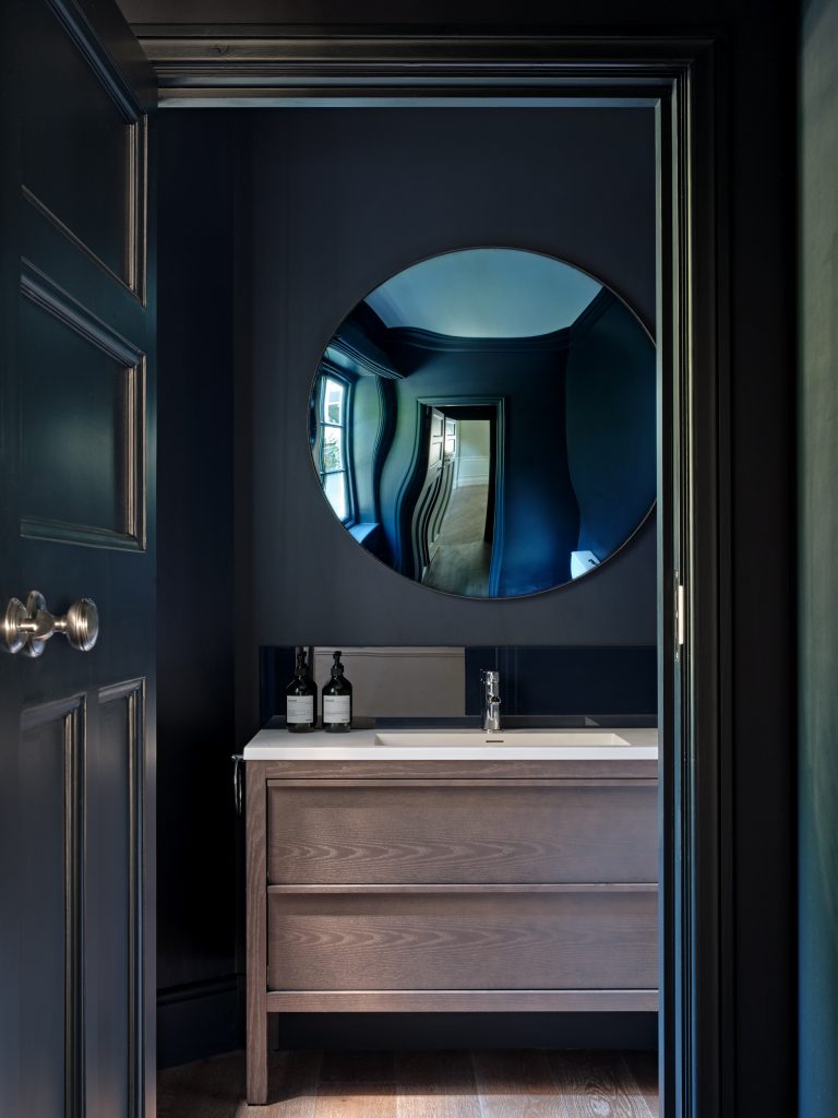 Dark blue cloakroom with bespoke vanity and circular mirror in Surrey Residence.