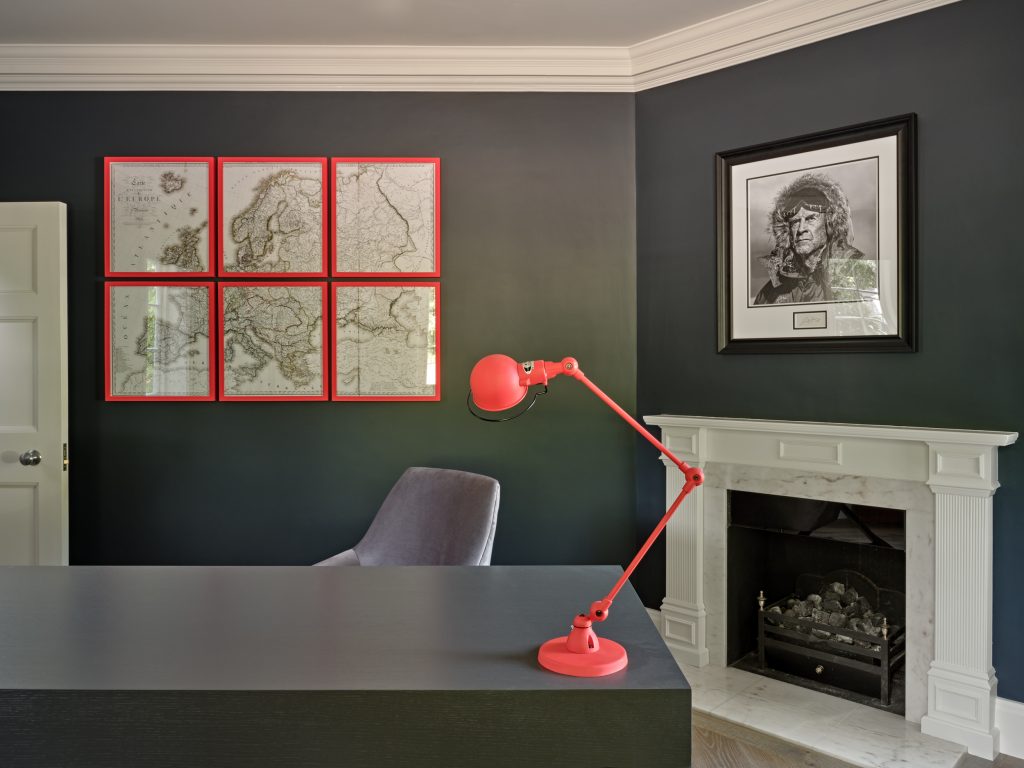 Dark blue home study with bespoke desk, marble fireplace and red accent lighting and picture frames in Surrey Residence.