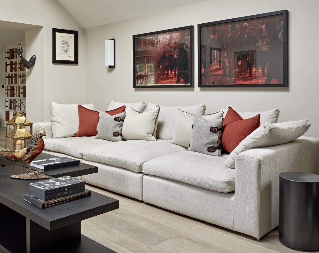 Neutral-toned living room with a large upholstered sofa styled with layered cushions, abstract artwork above, and dark coffee tables creating a calm, contemporary Cotswold retreat feel.