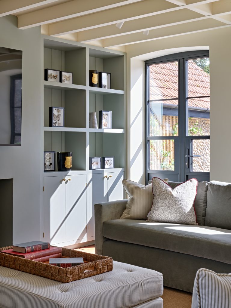 Light-filled sitting room in a Norfolk holiday home featuring bespoke shelving, a window seat and soft natural textures.